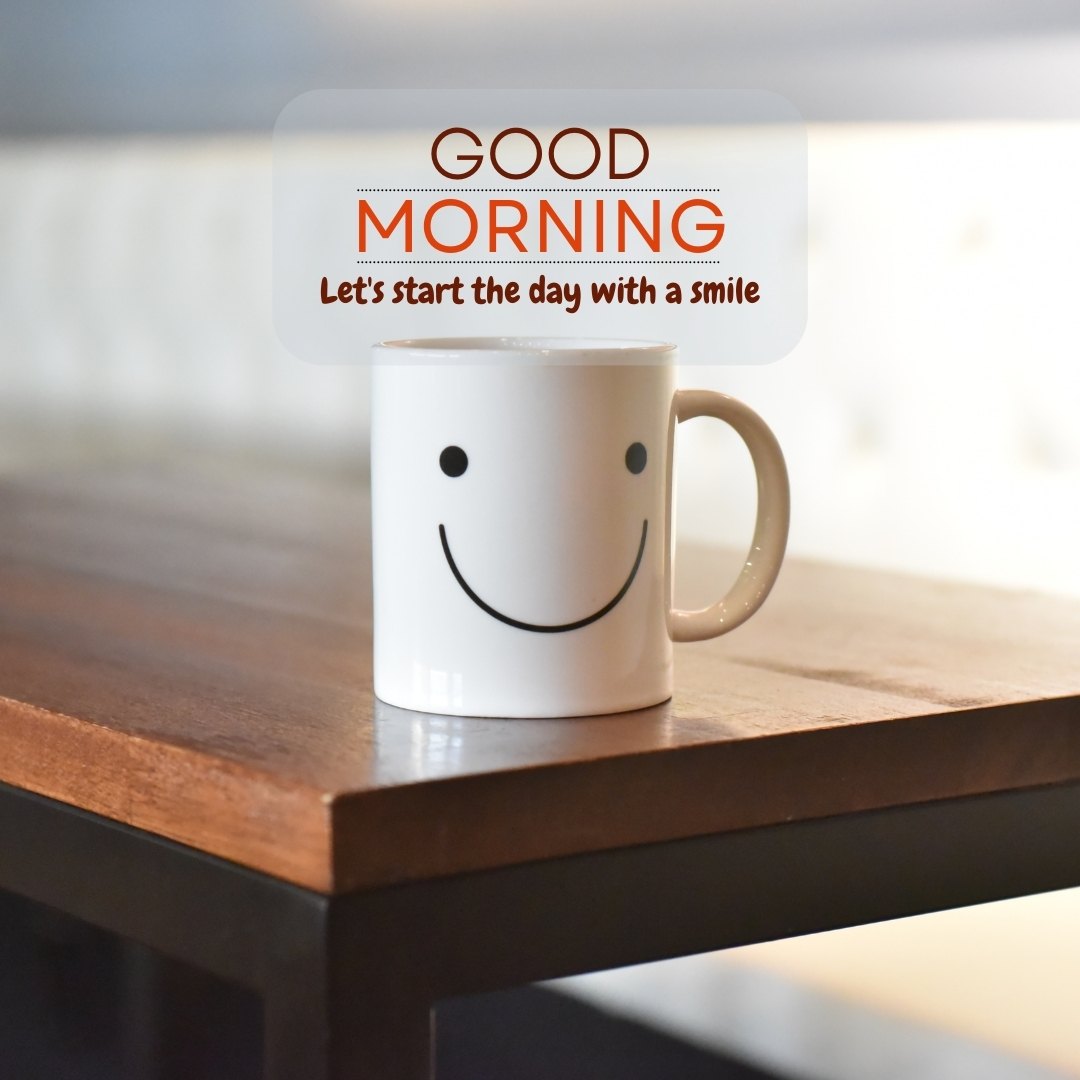 A cheerful white coffee mug with a smiling face design sits on a wooden table, under the words "GOOD MORNING" in orange, encouraging viewers to start the day with a smile. Perfect for posts about Sweet Good Morning Texts.